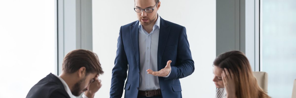 Angry male worker standing talking to colleagues lecturing on mistake in documents or failed project, businessman show dissatisfaction to business partner during negotiations or meeting in office