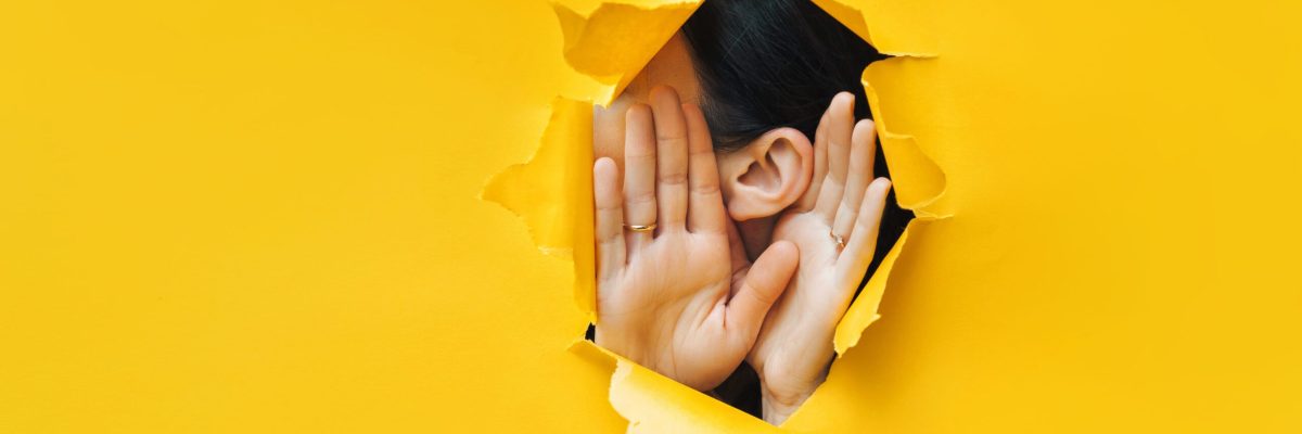 Female ear and hands close-up. Copy space. Torn paper, yellow background. The concept of eavesdropping, espionage, gossip and the yellow press.
