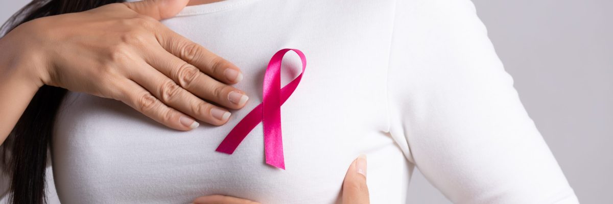 Closeup of pink badge ribbon on woman chest to support breast cancer cause. Healthcare, medicine and breast cancer awareness concept.
