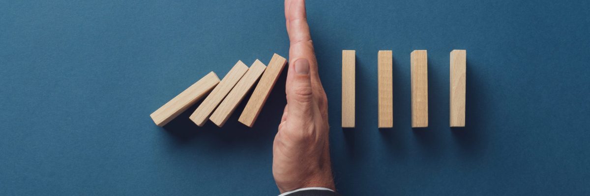 Top view of business crisis manager stopping falling dominos from collapsing. Over navy blue background.