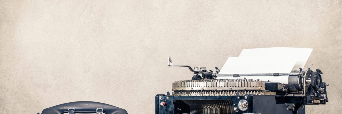 Retro old black telephone and aged typewriter with paper blank on wooden desk front concrete wall background. Vintage style filtered photo
