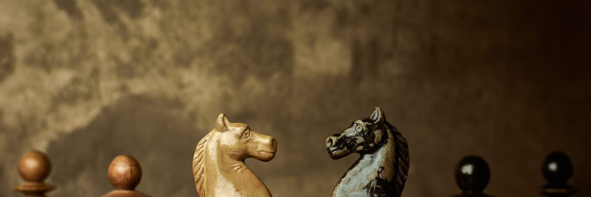 Wooden knights chess pieces facing each other on a vintage chessboard, rivalry concept.